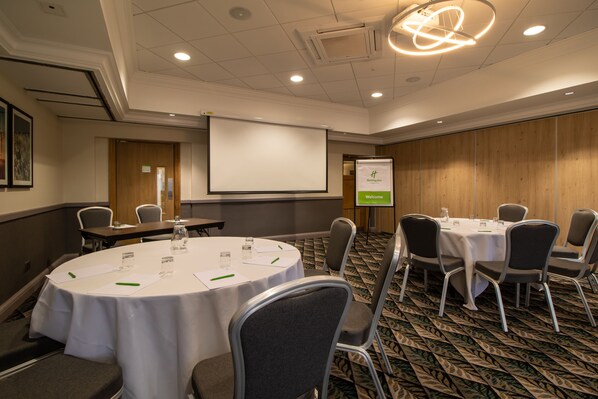 A conference room with round tables, chairs, a projector screen, and a welcome sign.