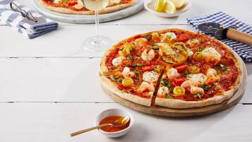 Due pizze su assi di legno, un bicchiere di vino bianco, mezzo limone e una piccola ciotola di salsa su un tavolo in legno chiaro.