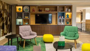 A modern living room with a flat-screen TV, wooden shelves with various decorative items, and comfortable seating including a purple armchair, a green armchair, and a yellow ottoman. - Holiday Inn Leicester - Wigston by IHG (Wigston)