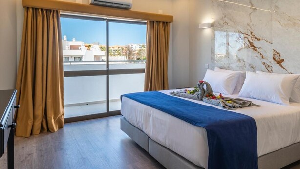Ein Hotelzimmer mit Bett, Schreibtisch, einem fensterbelaubten Fenster, einer Klimaanlage und einer Marmorwand.