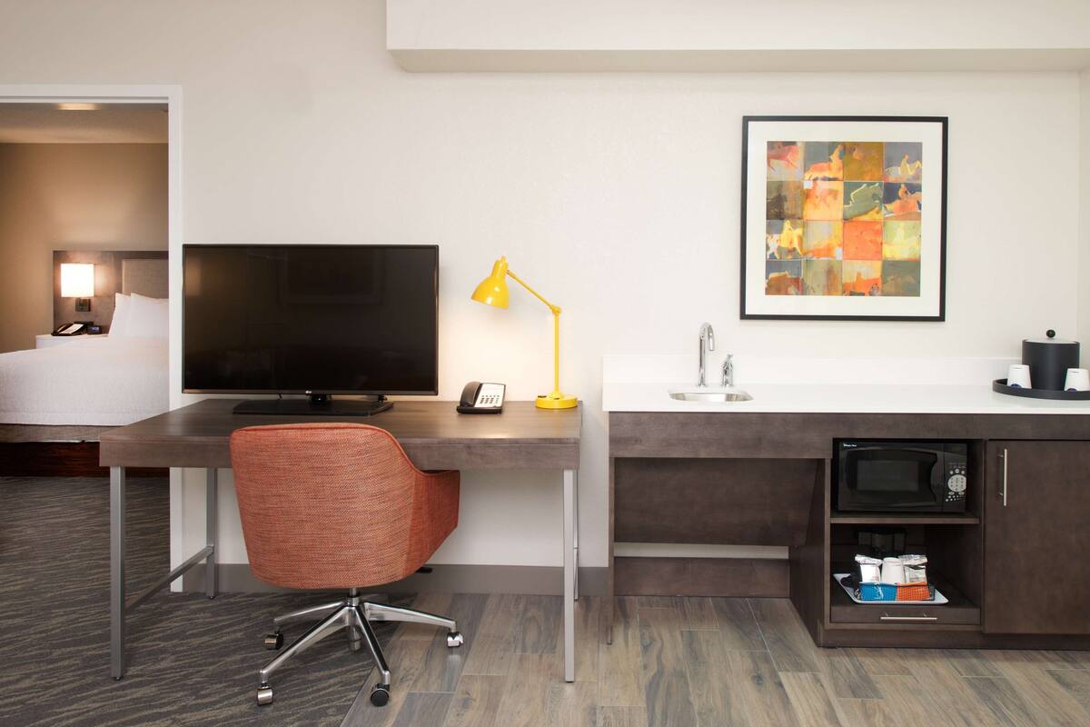 Hotelkamer met een bed, een bureau met een computer, een stoel, een bureaulamp, een wastafel, een magnetron en een kast met toiletartikelen.