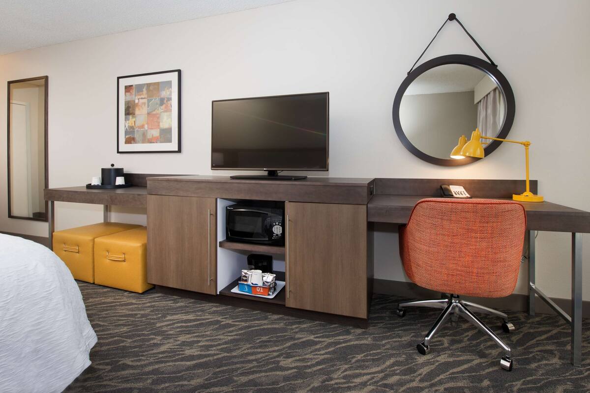 Hotelkamer met een bed, een bureau met een flatscreen televisie, een spiegel, een lamp en een stoel.