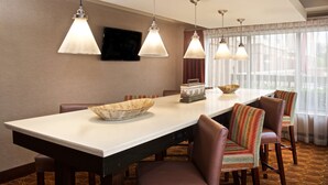 A modern dining area with a long table, multiple chairs, and pendant lighting. - Hampton Inn & Suites N. Ft. Worth-Alliance Airport (Fort Worth)