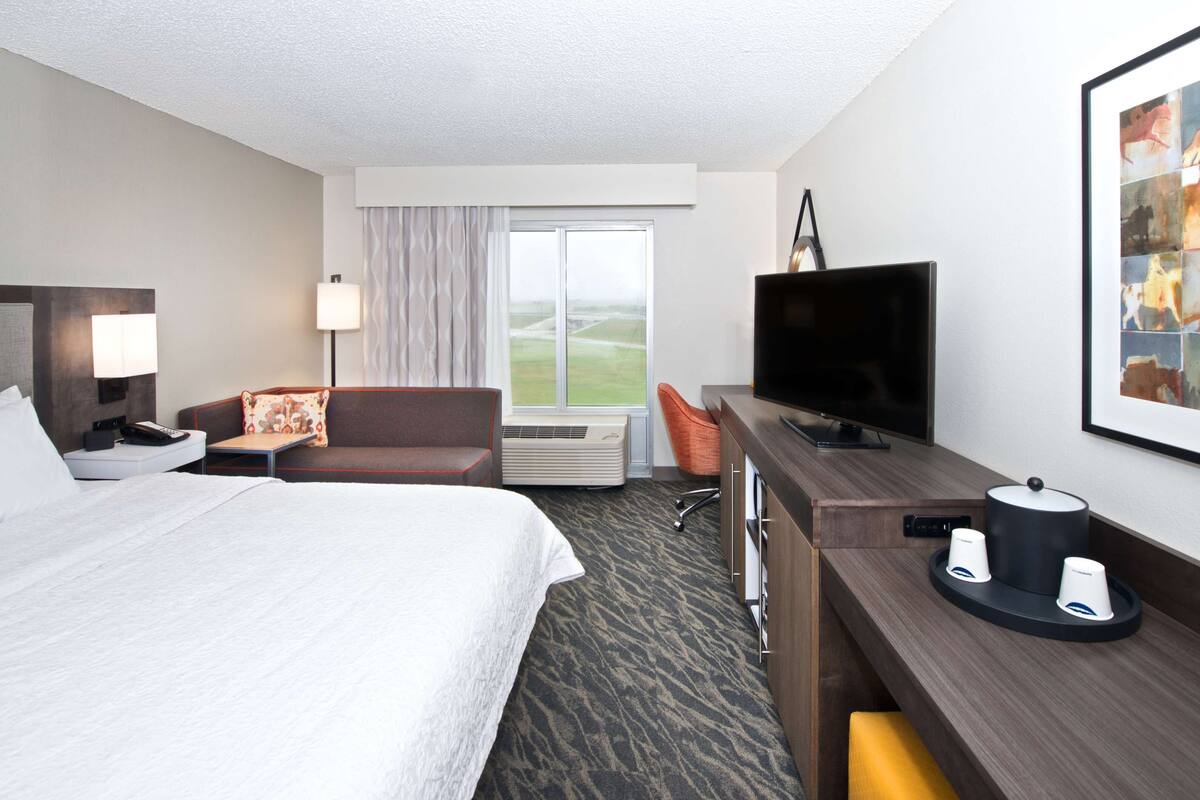 Hotelkamer met een bed, een bureau met televisie, een stoel, een lamp en een raam met gordijnen.