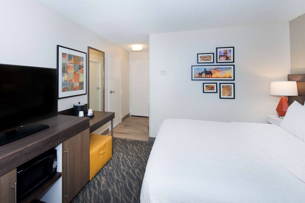 Hotelkamer met flatscreen televisie, bureau met lamp, bed en kunstwerk aan de muur.