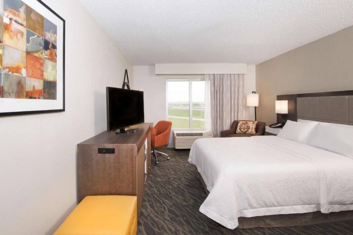 Een hotelkamer met een bed, een bureau, een stoel, een televisie en een raam met gordijnen.