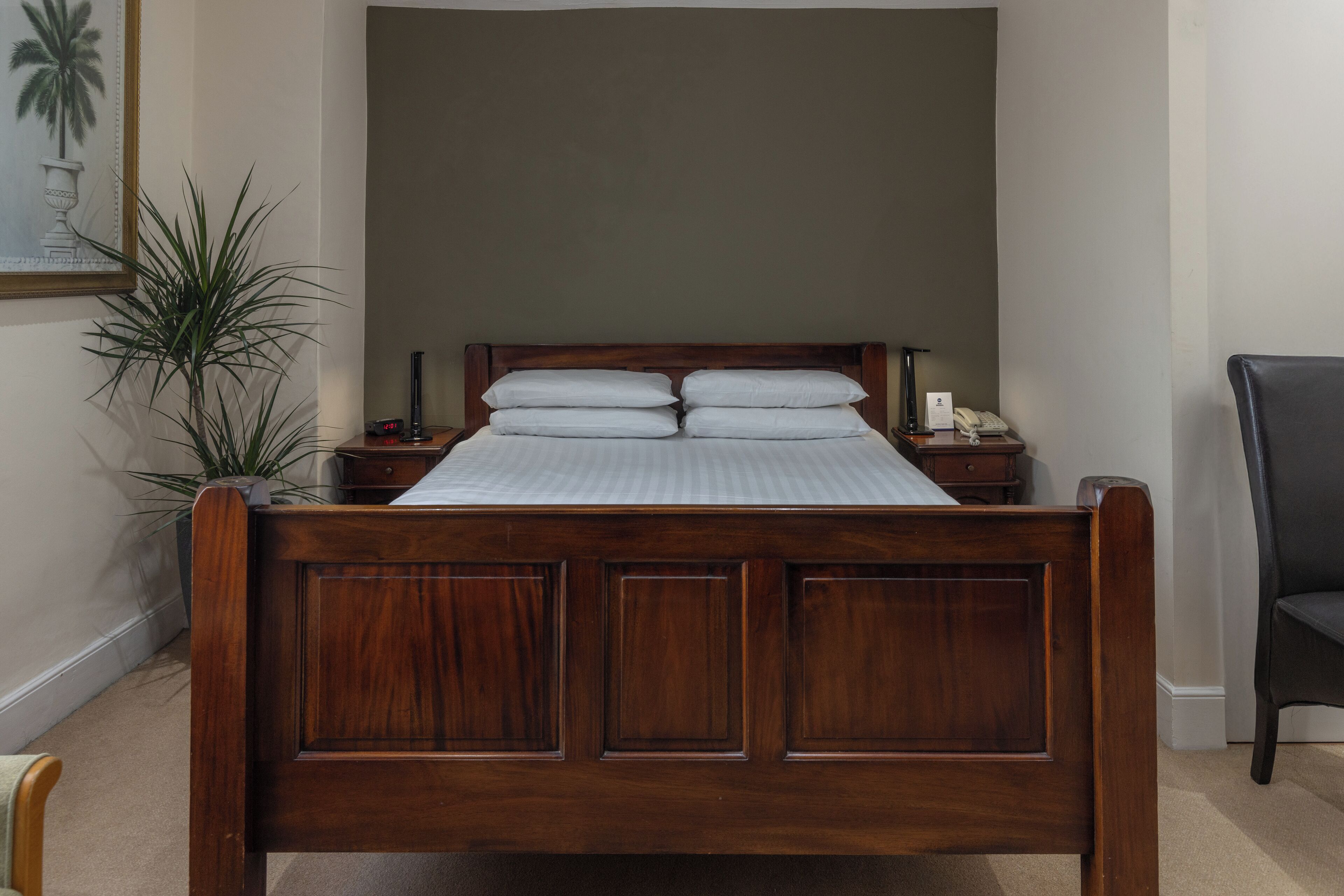 Una cama de madera con cabecera, dos mesitas de noche y un tocador con lámpara y teléfono.