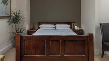 Una cama de madera con cabecera, dos mesitas de noche y un tocador con lámpara y teléfono.