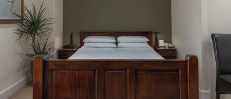 Una cama de madera con cabecera, dos mesitas de noche y un tocador con lámpara y teléfono.
