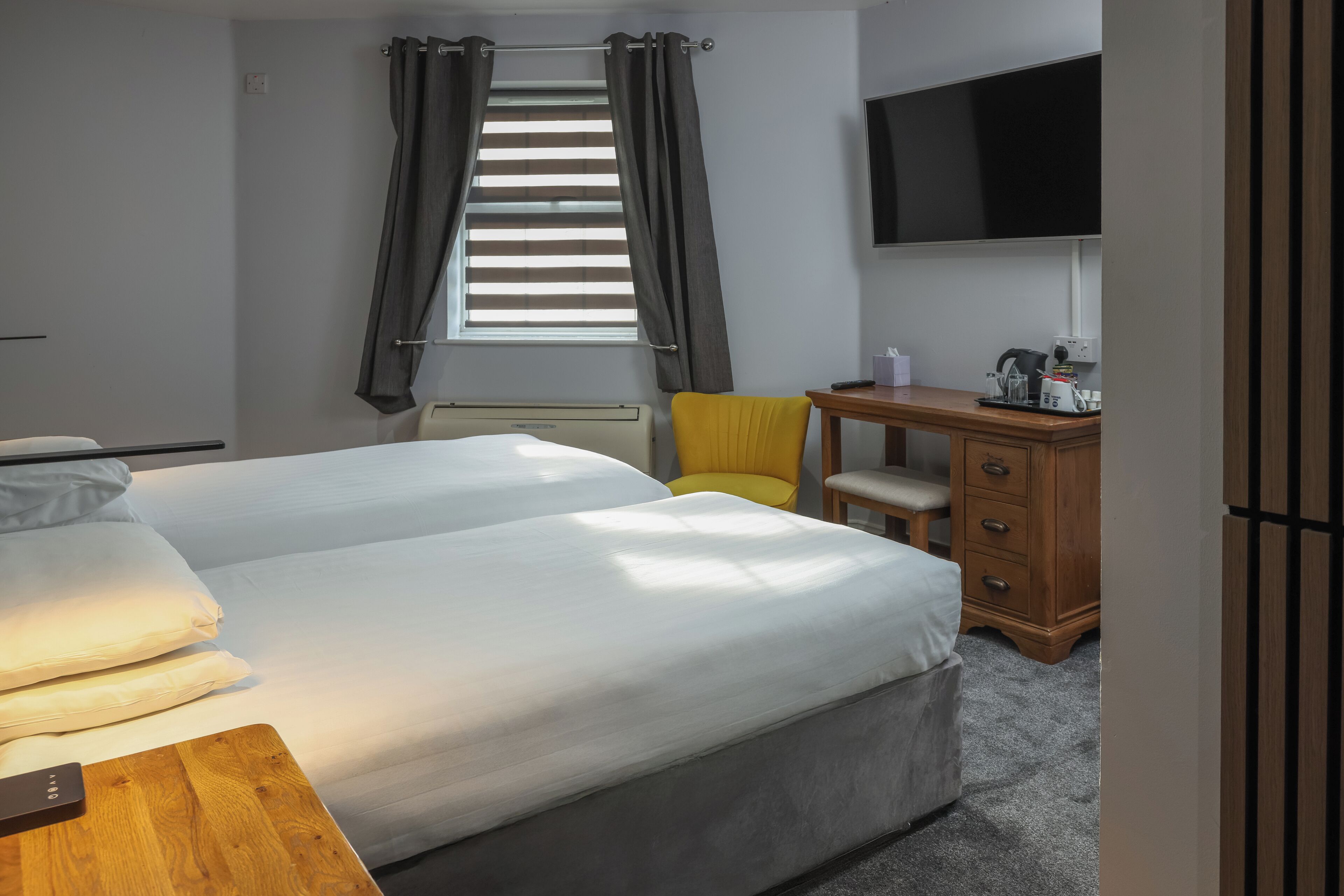 A hotel room with two beds, a desk, a chair, a TV, and a window with curtains.