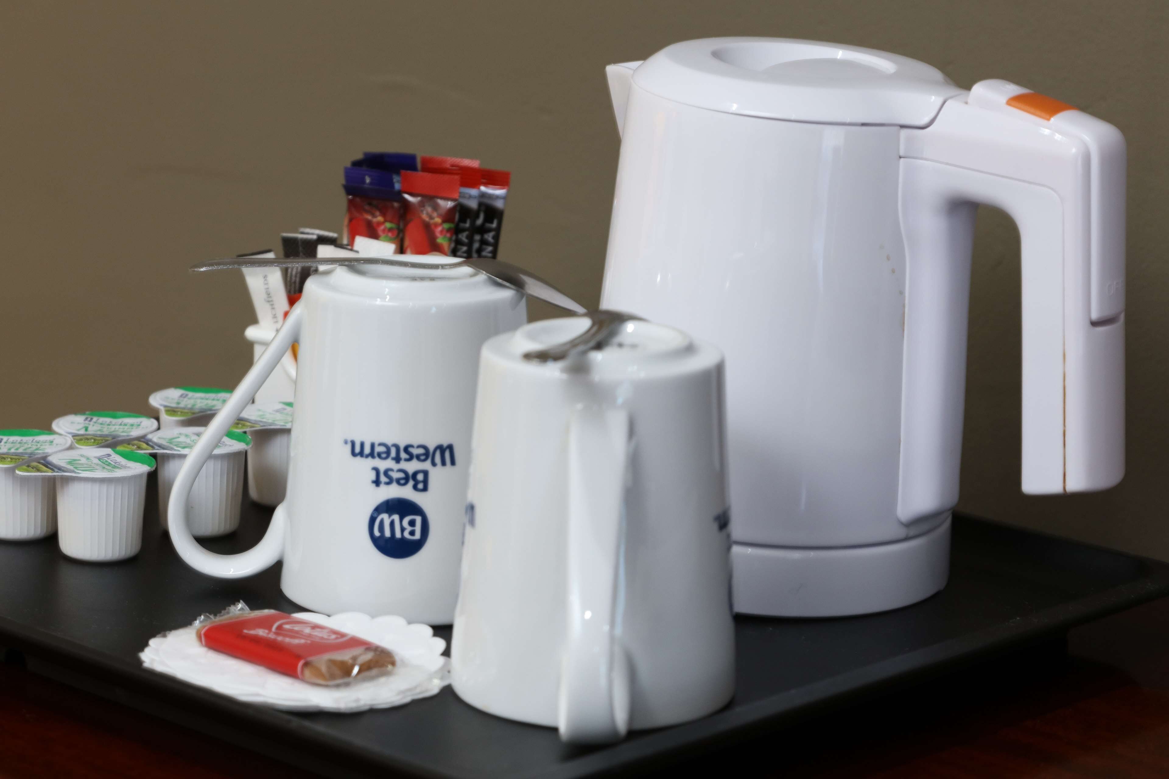 Une table avec une bouilloire blanche, une tasse blanche avec du texte bleu et plusieurs petits récipients.
