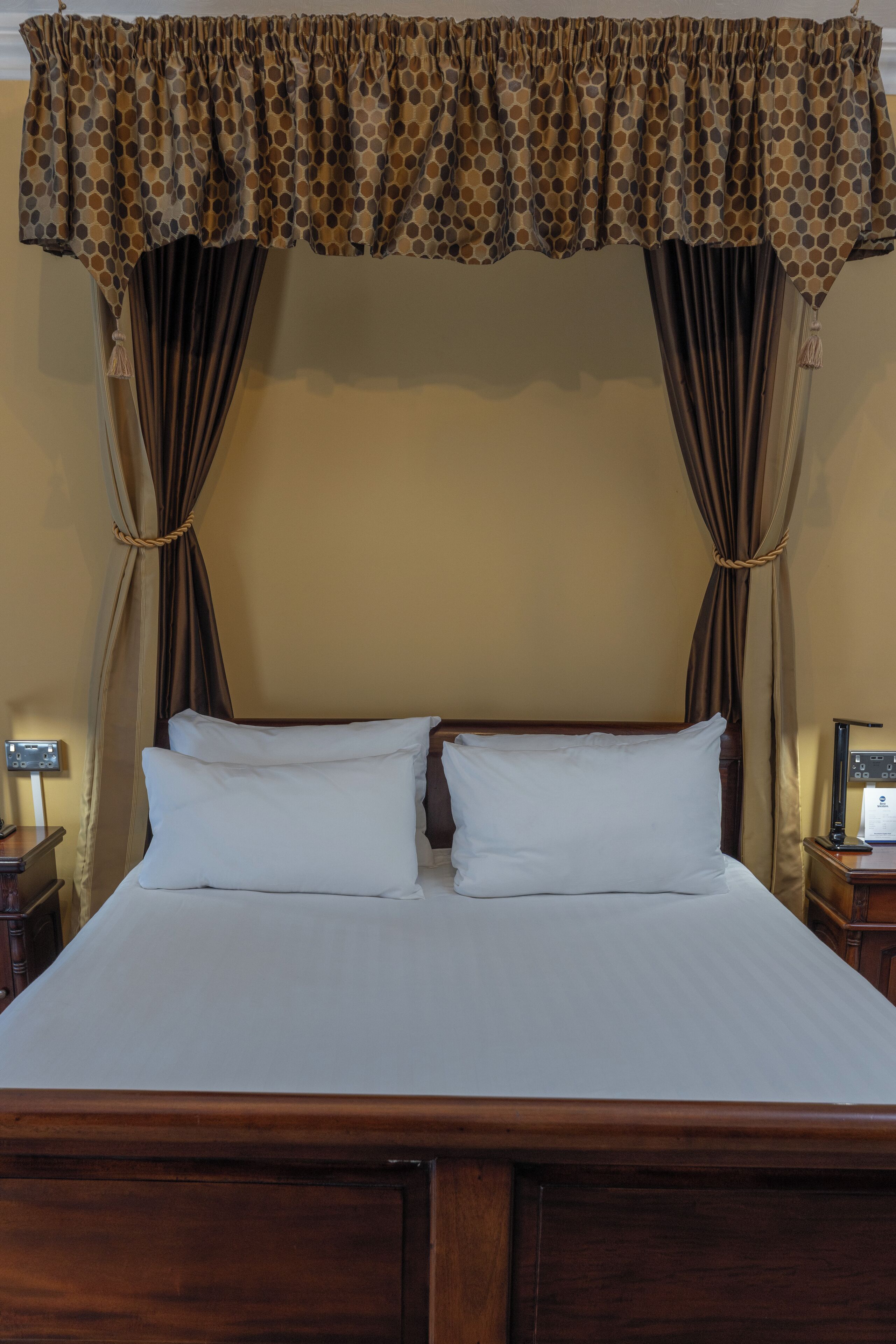 A bed with two white pillows, a wooden headboard, and a brown curtain with a polka dot pattern.