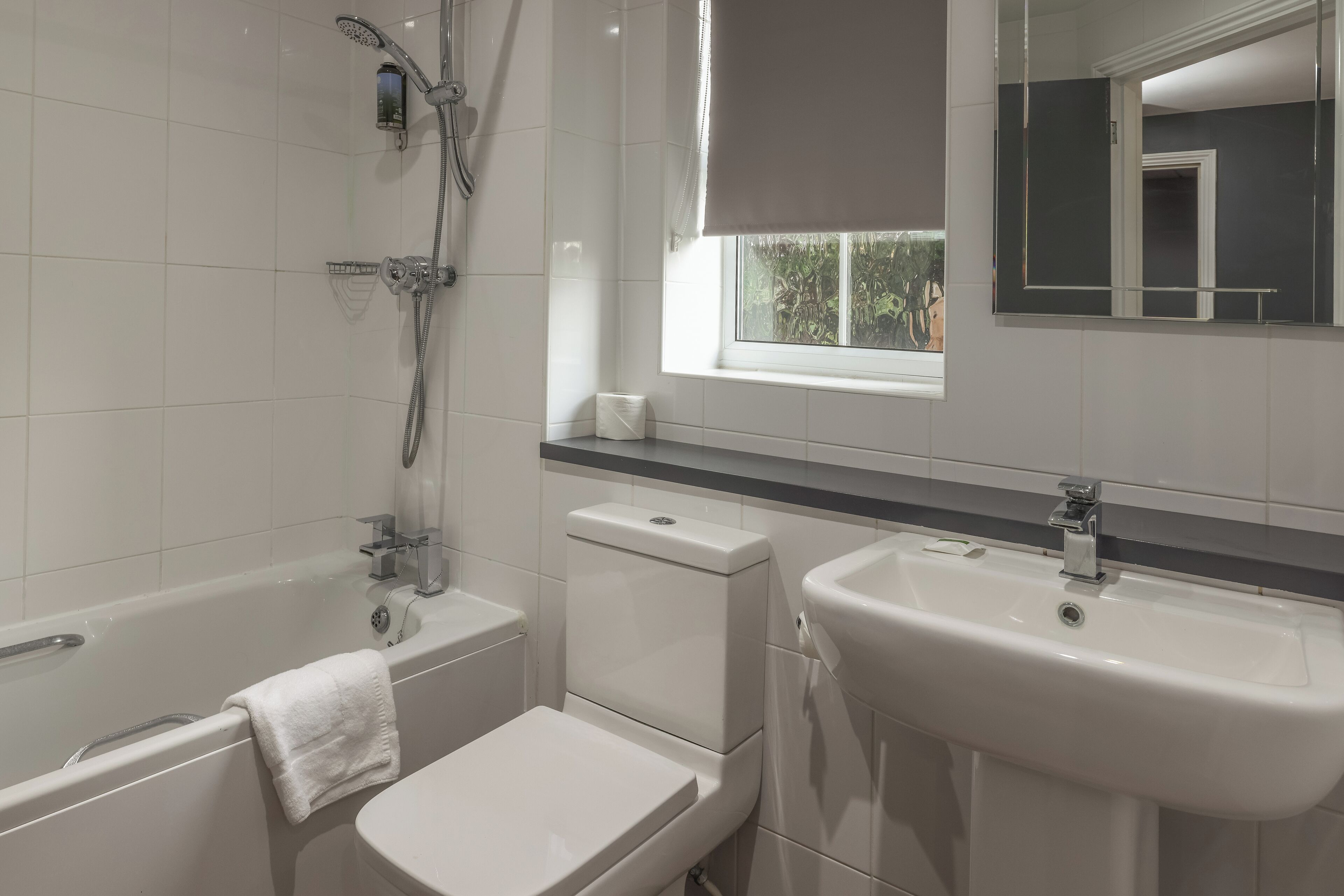 Ein Badezimmer mit Badewanne, Toilette, Waschbecken und einem Fenster mit Blick auf Grünflächen.