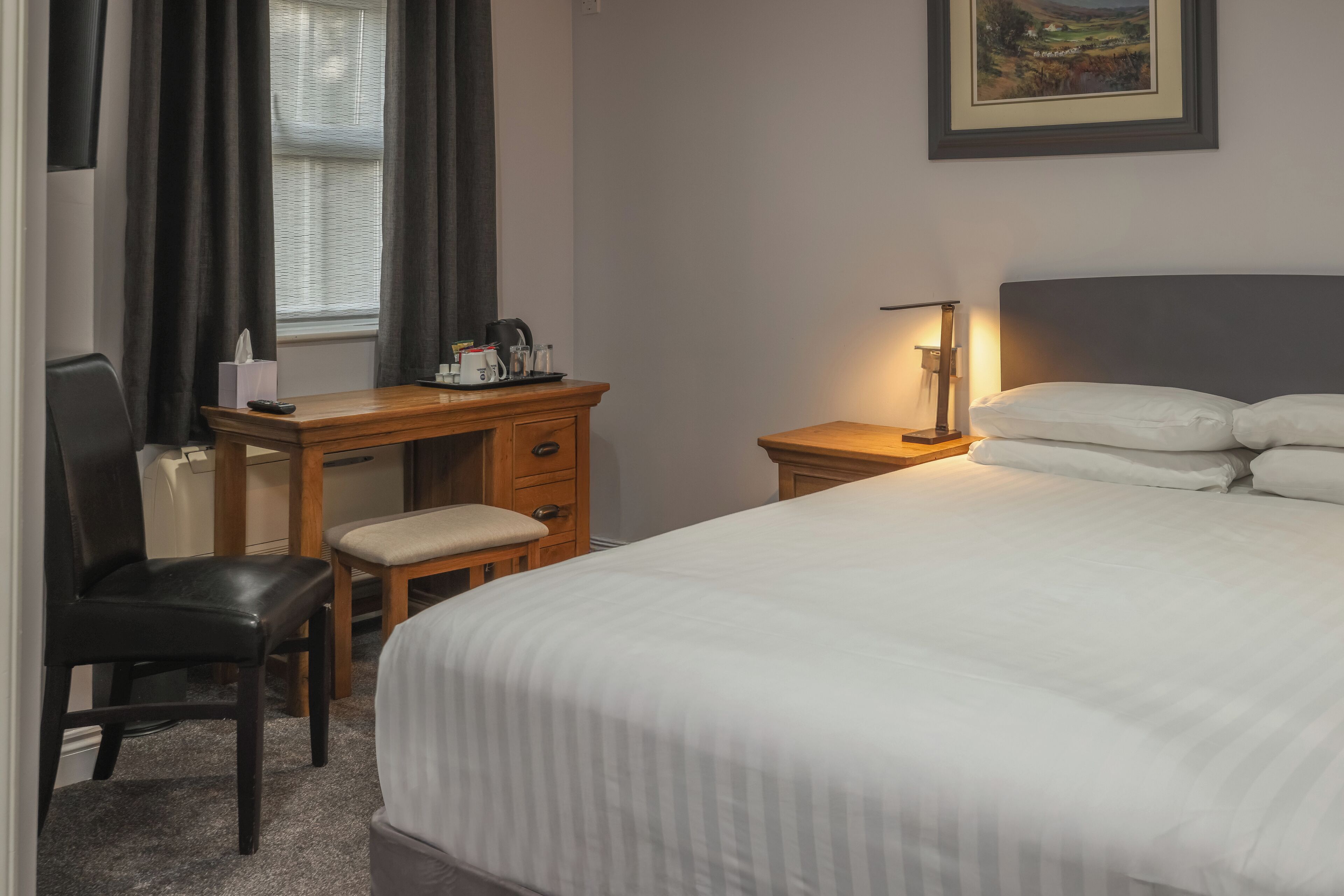 Una habitación de hotel con una cama, un escritorio con silla, una lámpara y una ventana con cortinas.