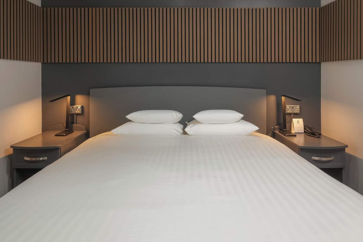 Ein modernes Hotelzimmer mit einem großen Bett, zwei Nachttischen und einer Wandleuchte.