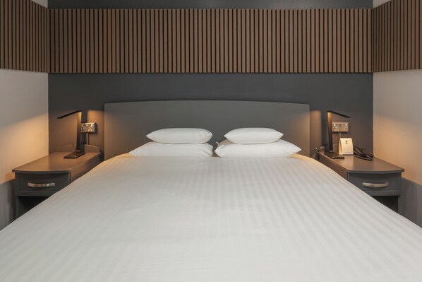 A modern hotel room with a large bed, two bedside tables, and a wall-mounted light fixture.