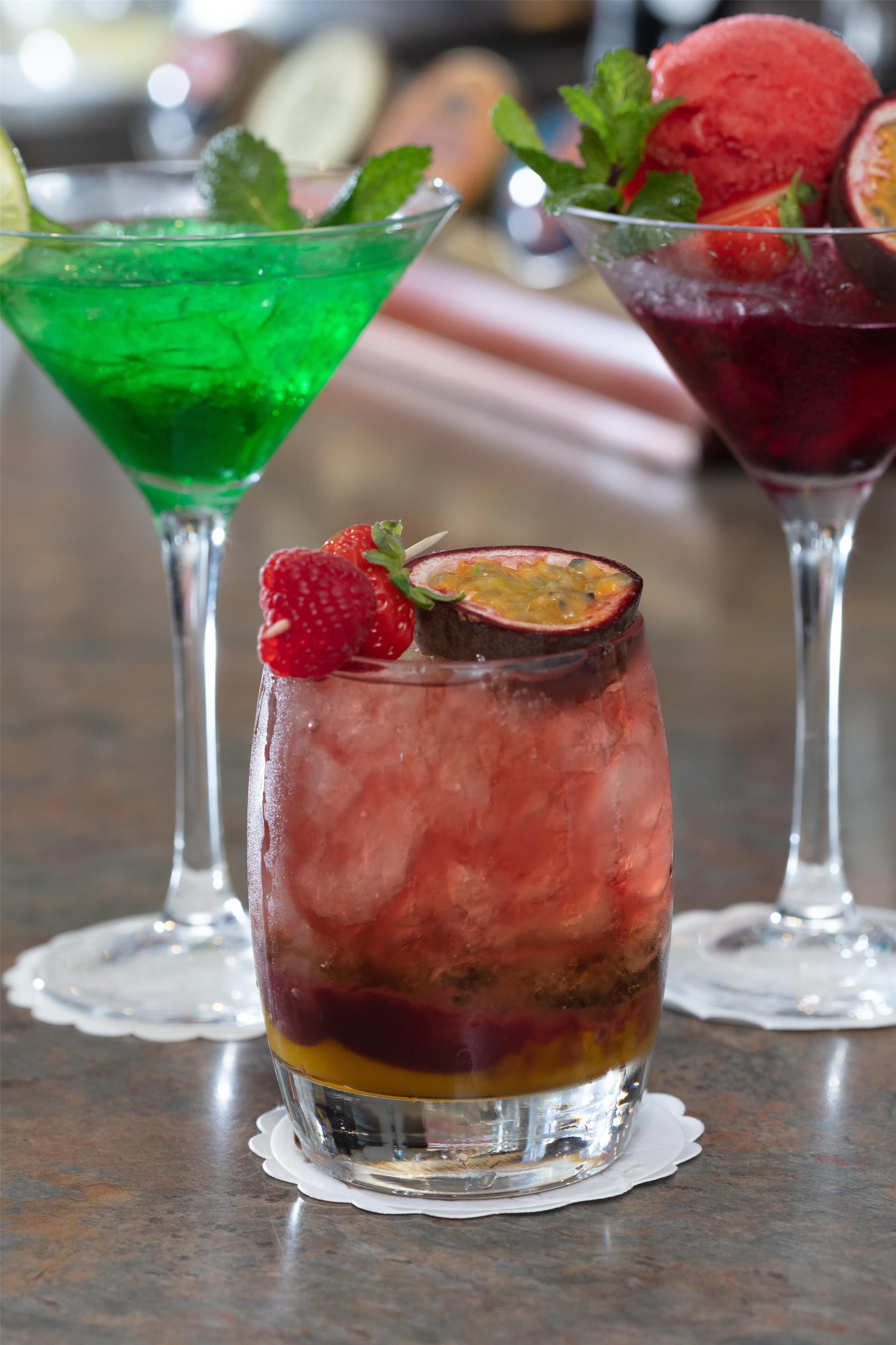 Drie cocktails in martini glazen met ijs, versierd met aardbeien en muntblaadjes.
