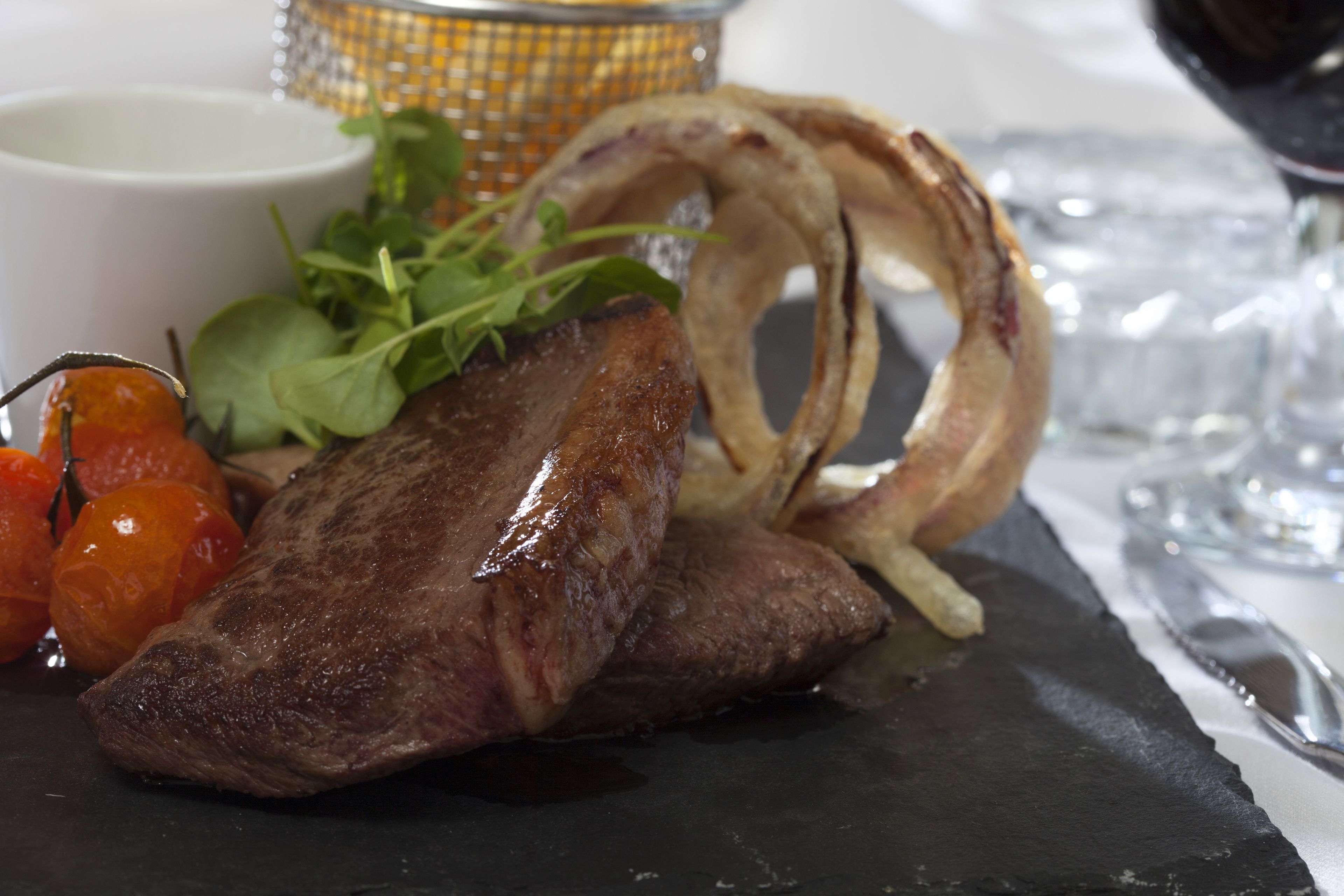 Ein Teller Essen mit Steak, Cocktailtomaten und Zwiebelringen.