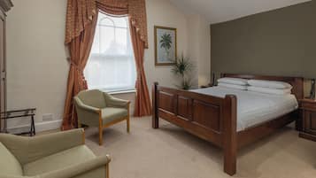 Un dormitorio con una cama de madera, un sillón verde, una ventana con cortinas y un cuadro enmarcado en la pared.