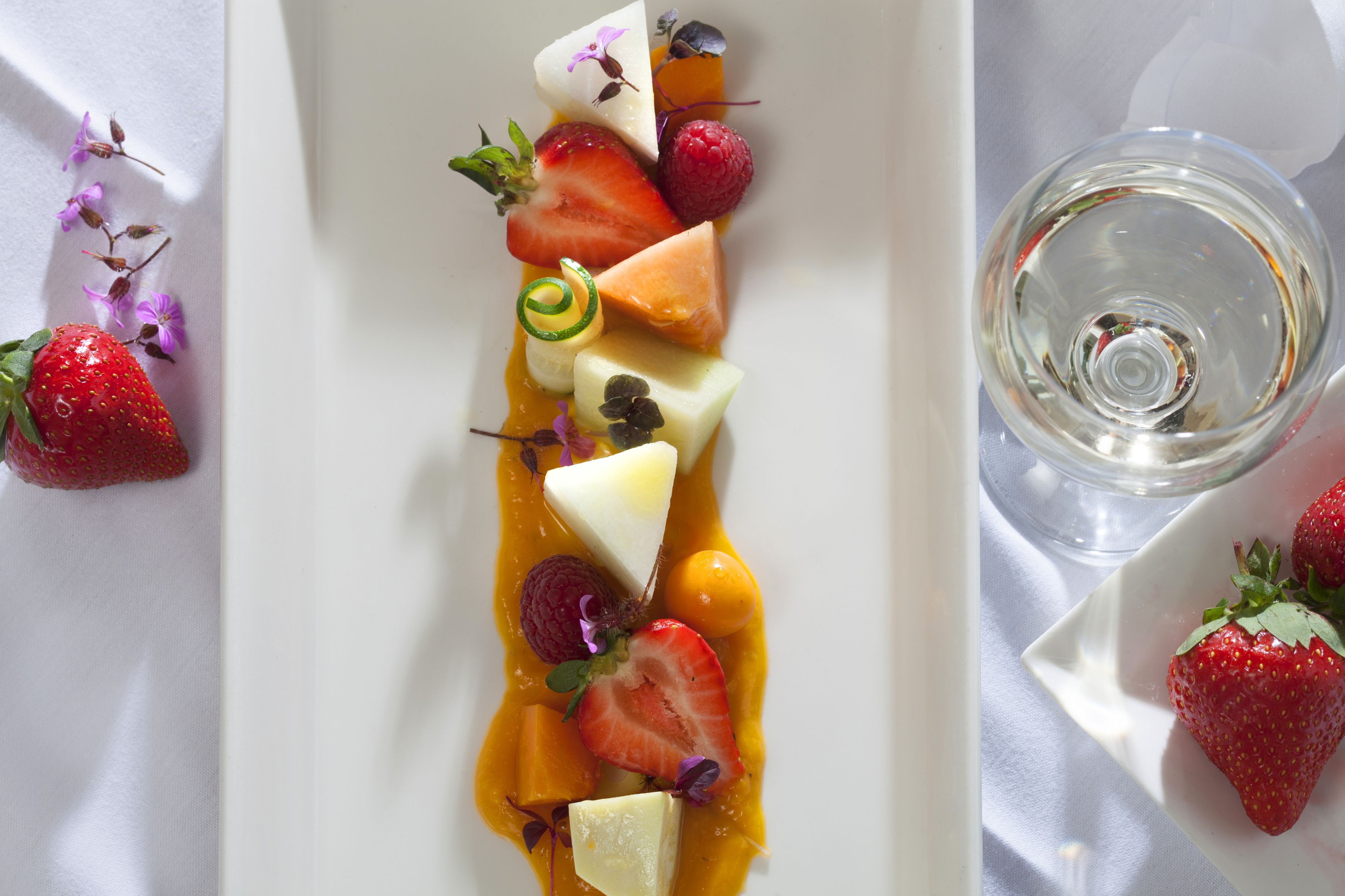 A white plate with a variety of fruits and a glass of water.