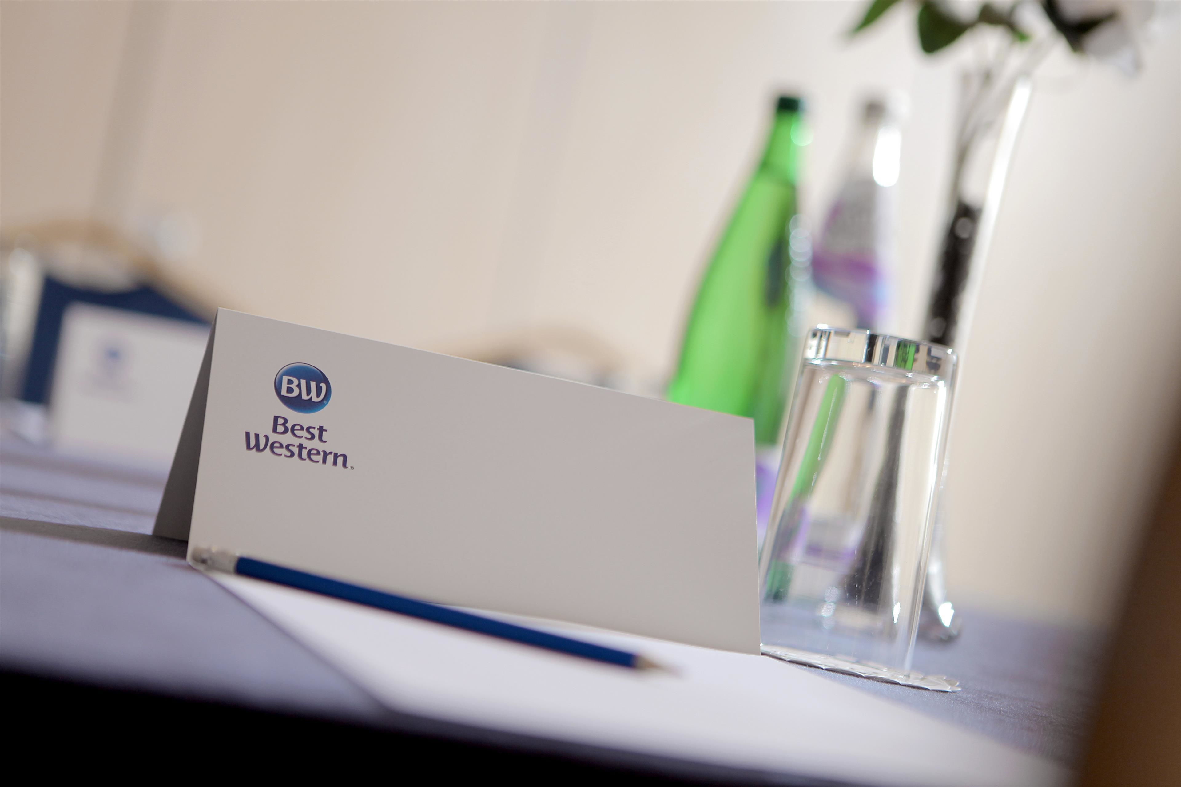A hotel name card labeled "Best Western" on a table with a glass of water and a pen.