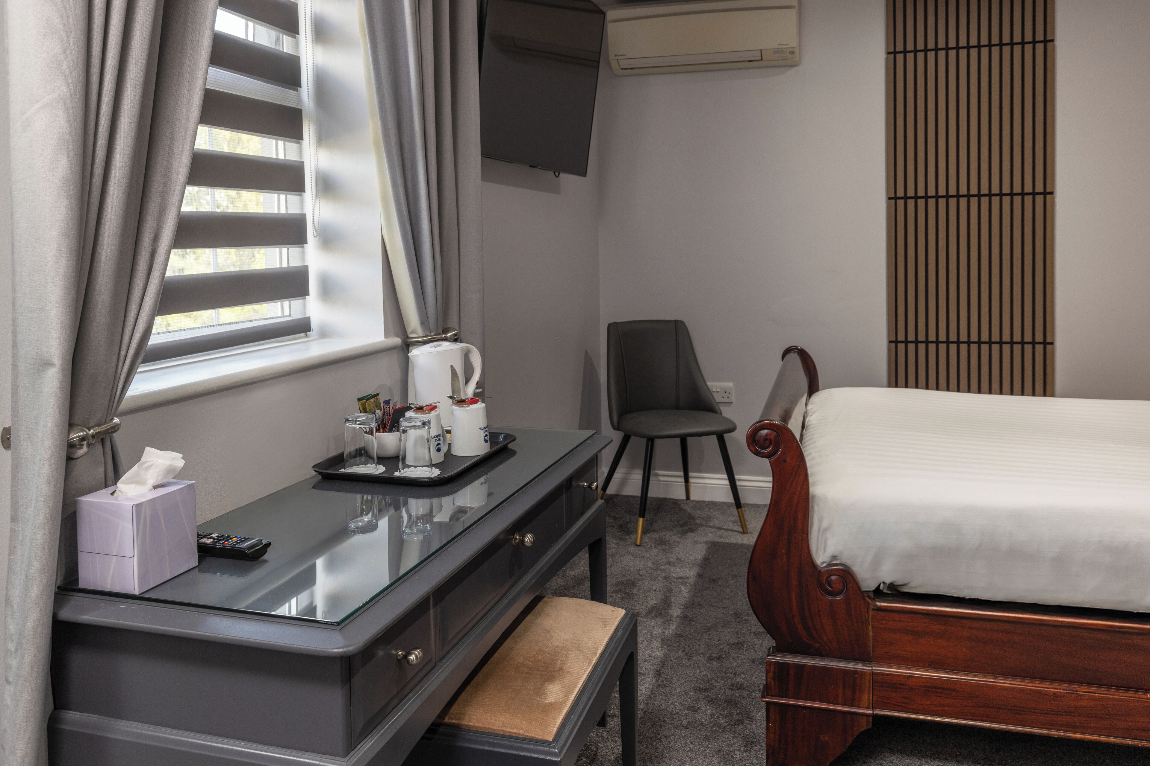 A hotel room with a bed, a desk with a tray of toiletries, a chair, and a window with curtains.