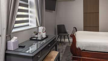 Habitación de hotel con cama, escritorio, bandeja de artículos de aseo, una silla y ventana con cortinas.