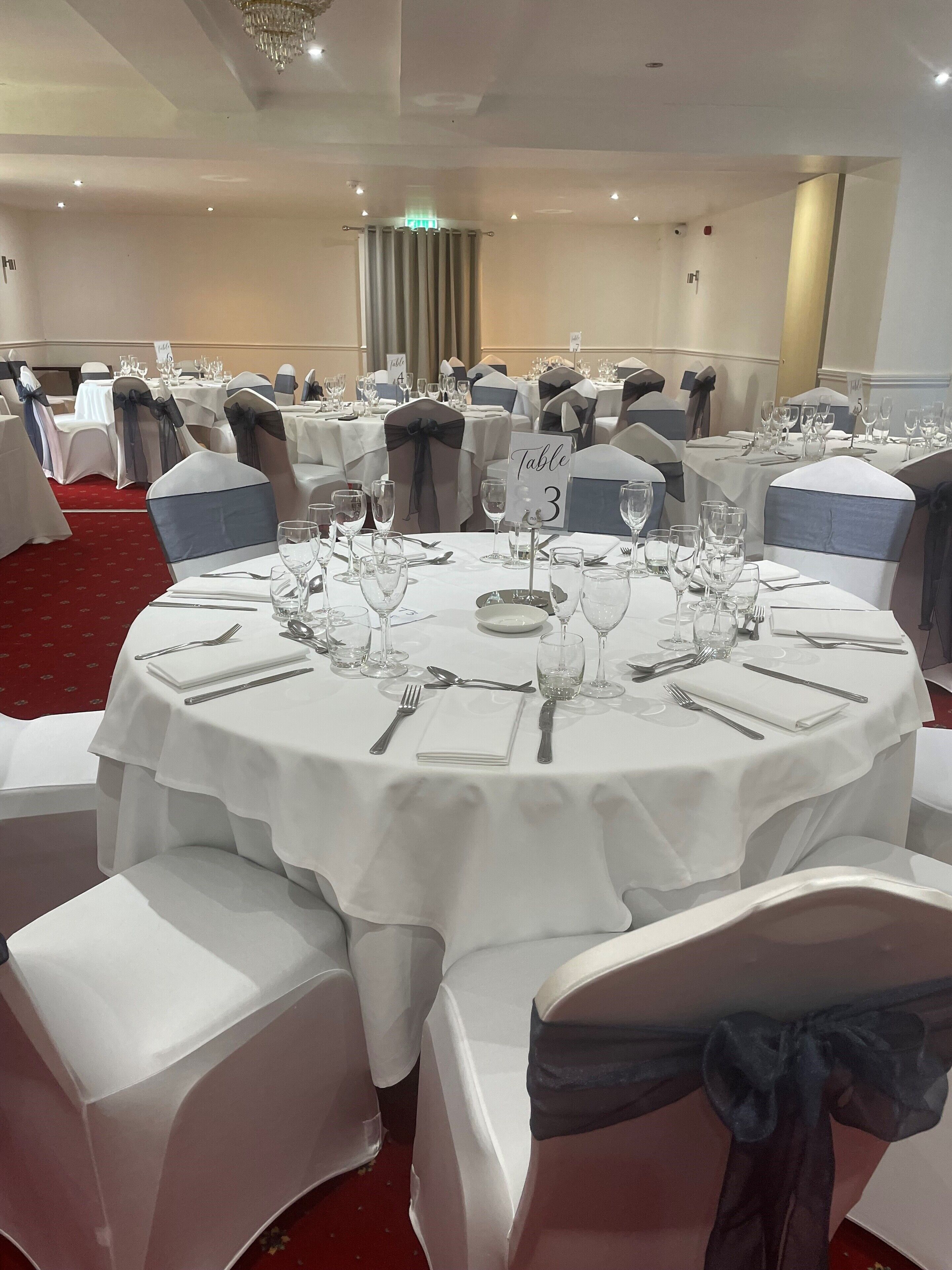 A banquet hall with round tables set for a formal event, each with white tablecloths, silverware, and glassware.