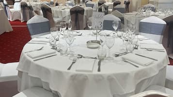 A banquet hall with round tables set for a formal event, each with white tablecloths, silverware, and glassware.