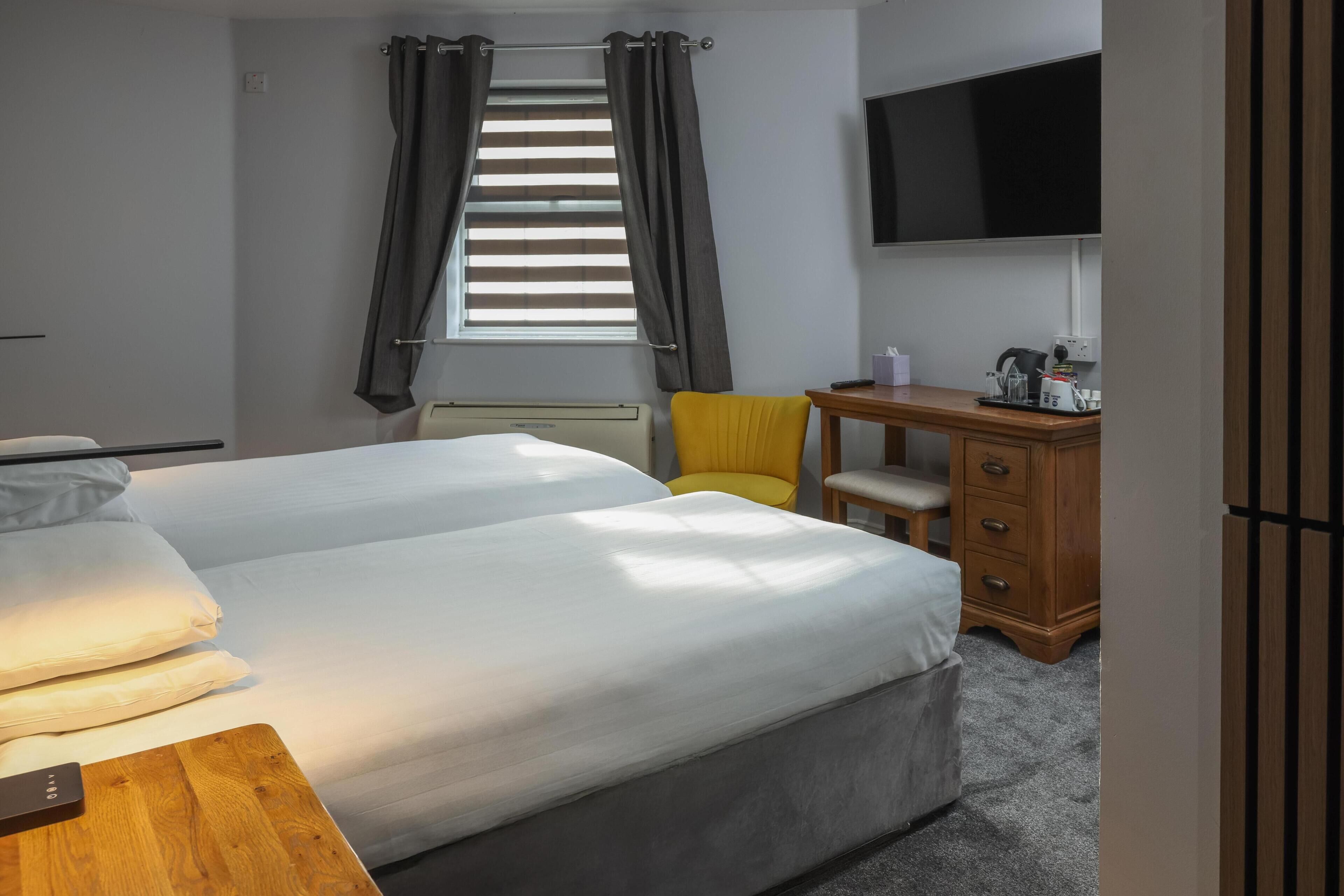 A hotel room with two beds, a desk, a chair, a TV, and a window with curtains.
