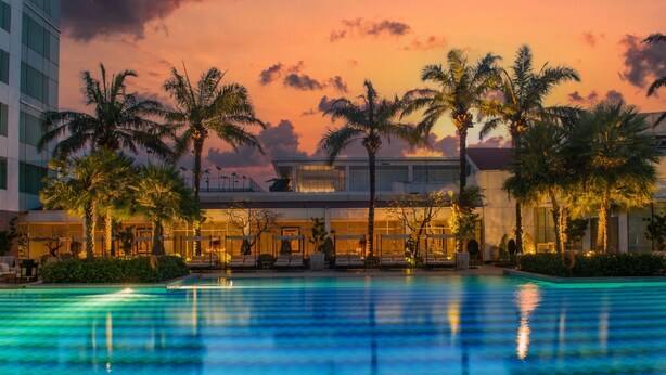 Un hotel con piscina, palme e un cielo al tramonto.