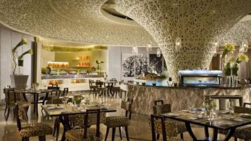 A modern restaurant with a unique ceiling design, a bar area, and a variety of seating arrangements.