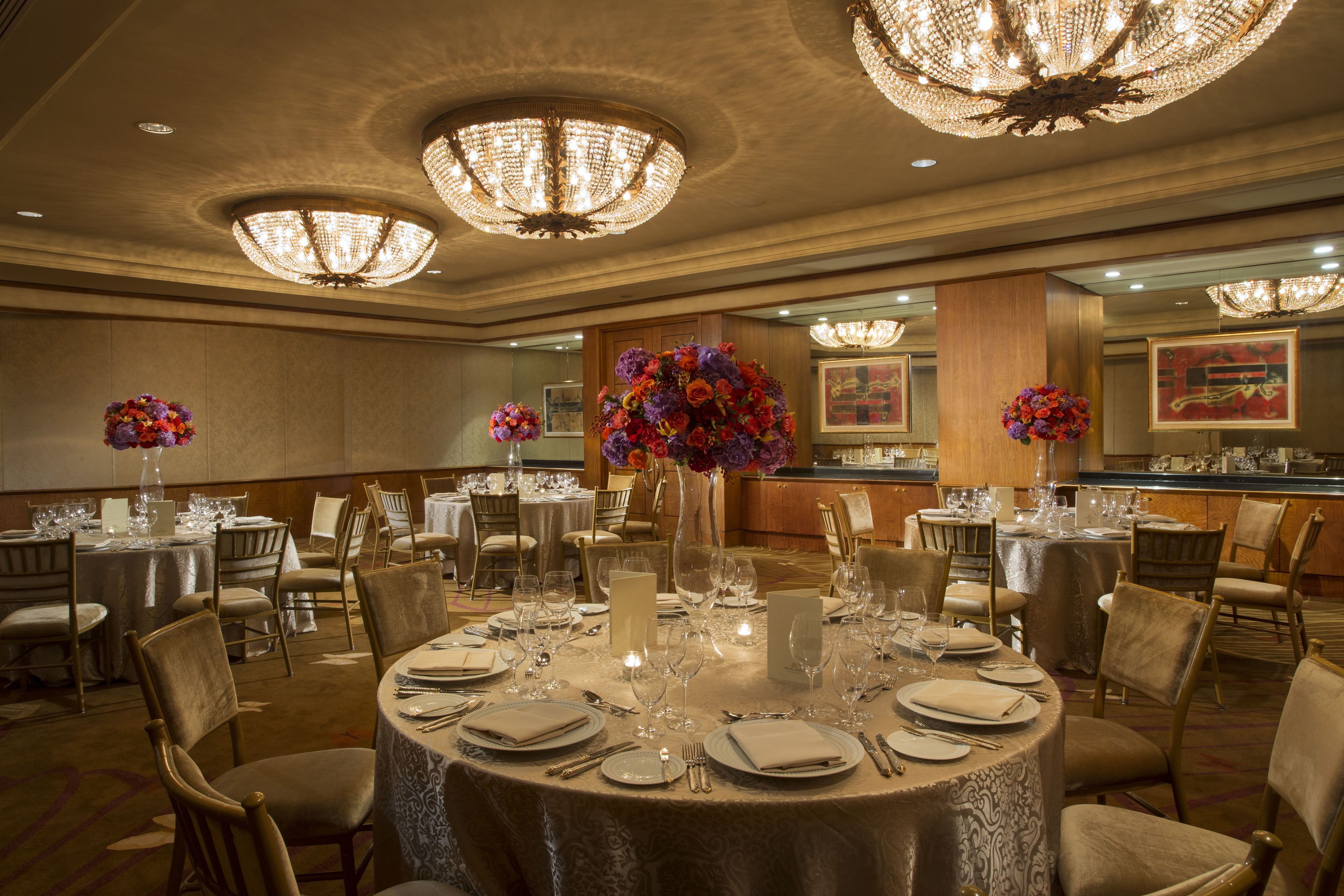 Un salón de banquetes con mesas redondas dispuestas para cenar, candelabros y centros de mesa florales.