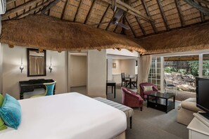 Habitación de hotel con una cama grande, un escritorio, una silla, un televisor y un comedor con mesa y sillas.