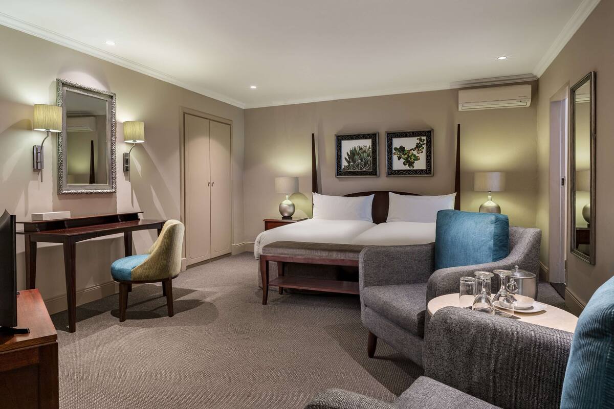 Ein Hotelzimmer mit Bett, Schreibtisch, Sessel, Sofa und einem kleinen Tisch mit Gläsern und einer Karaffe.