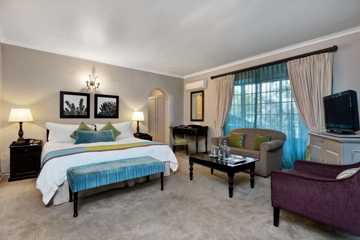 A hotel room with a bed, a sofa, a coffee table, a television, and a desk.