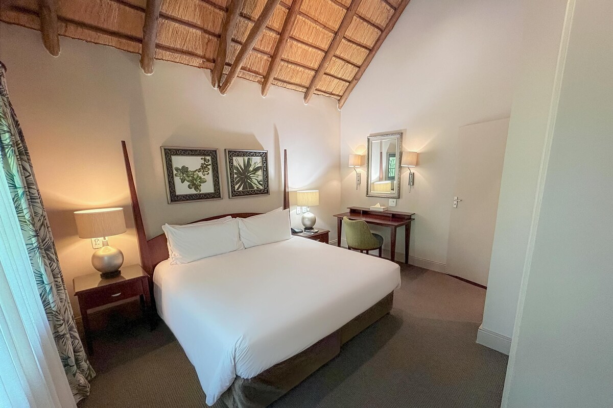 Une chambre d’hôtel avec un grand lit, un bureau, une chaise, un miroir et deux lampes fixées au mur.