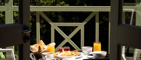 Bandeja de desayuno con cruasanes, fruta y bebidas sobre una mesa junto a una ventana.