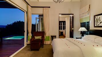 A hotel room with a large bed, a chair, a small table, a lamp, and a view of a swimming pool.