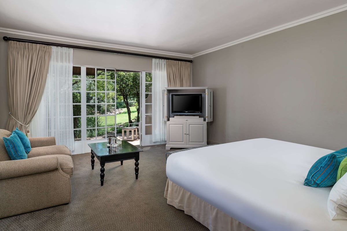 Ein Hotelzimmer mit einem großen Bett, einer Couch, einem Fernseher auf einem Schrank und Blick auf einen Garten durch das Fenster.