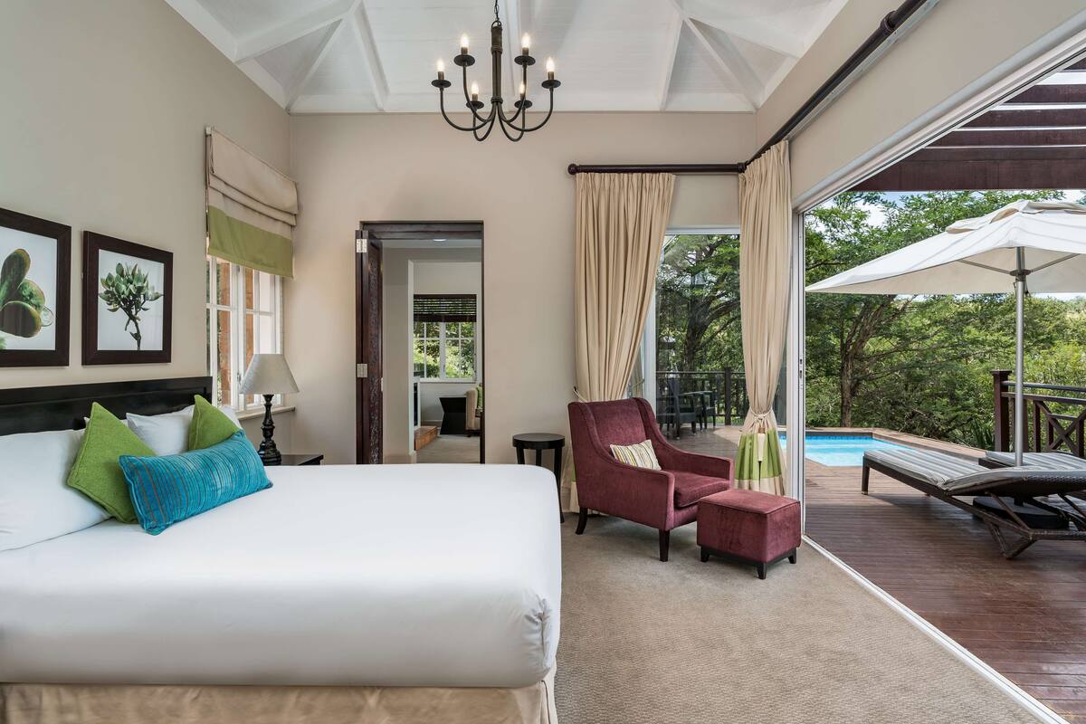 Ein Hotelzimmer mit einem großen Bett, einem Sessel, einem kleinen Tisch und Blick auf einen Außenpool.