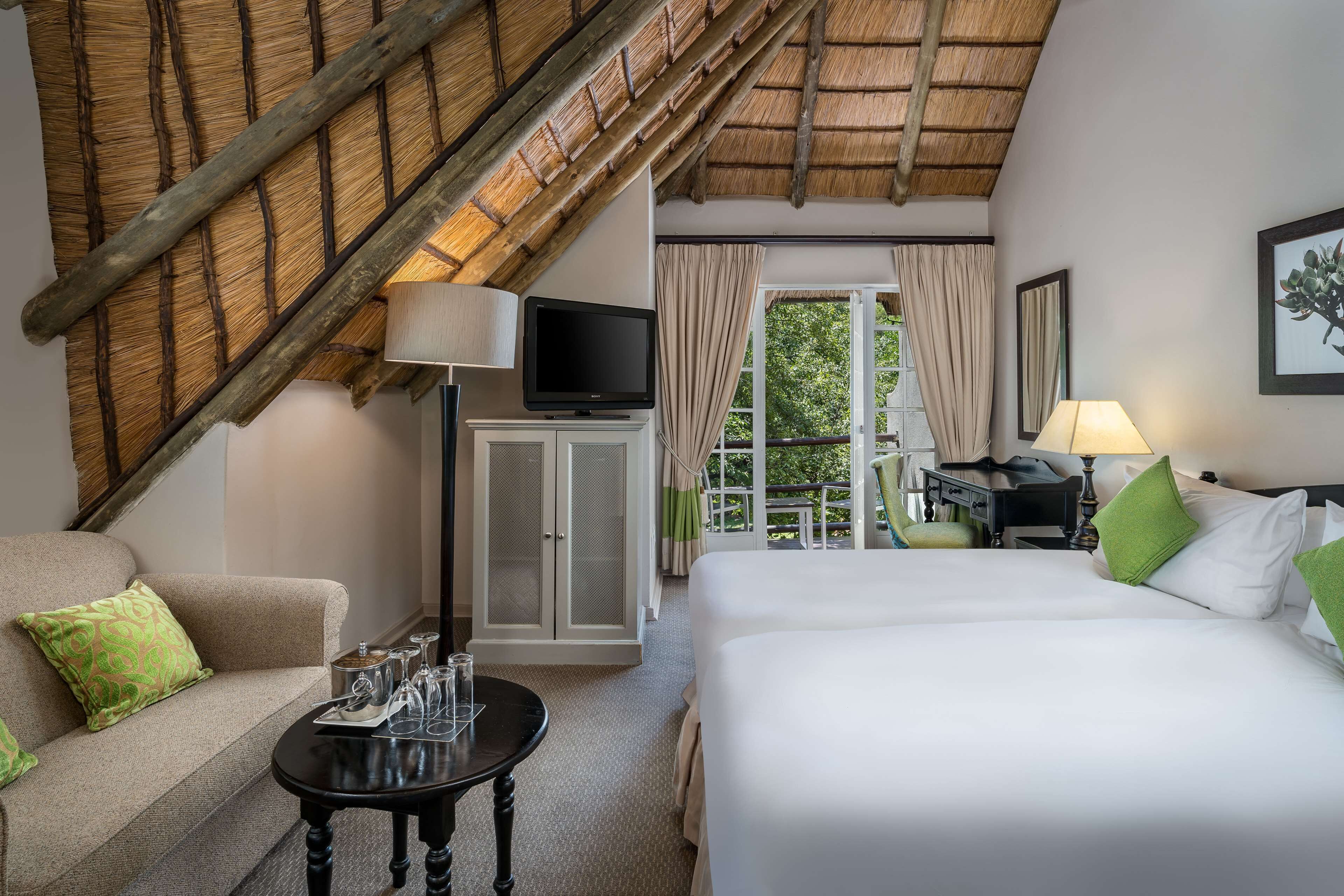 Habitación de hotel con cama, sofá, televisor, escritorio y ventana con cortinas.