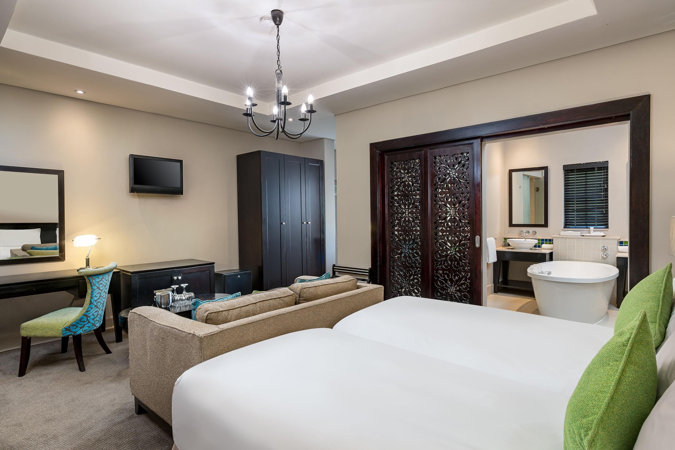 A hotel room with a bed, a desk with a chair, a television, a wardrobe, a bathroom with a sink and mirror, and a decorative door.