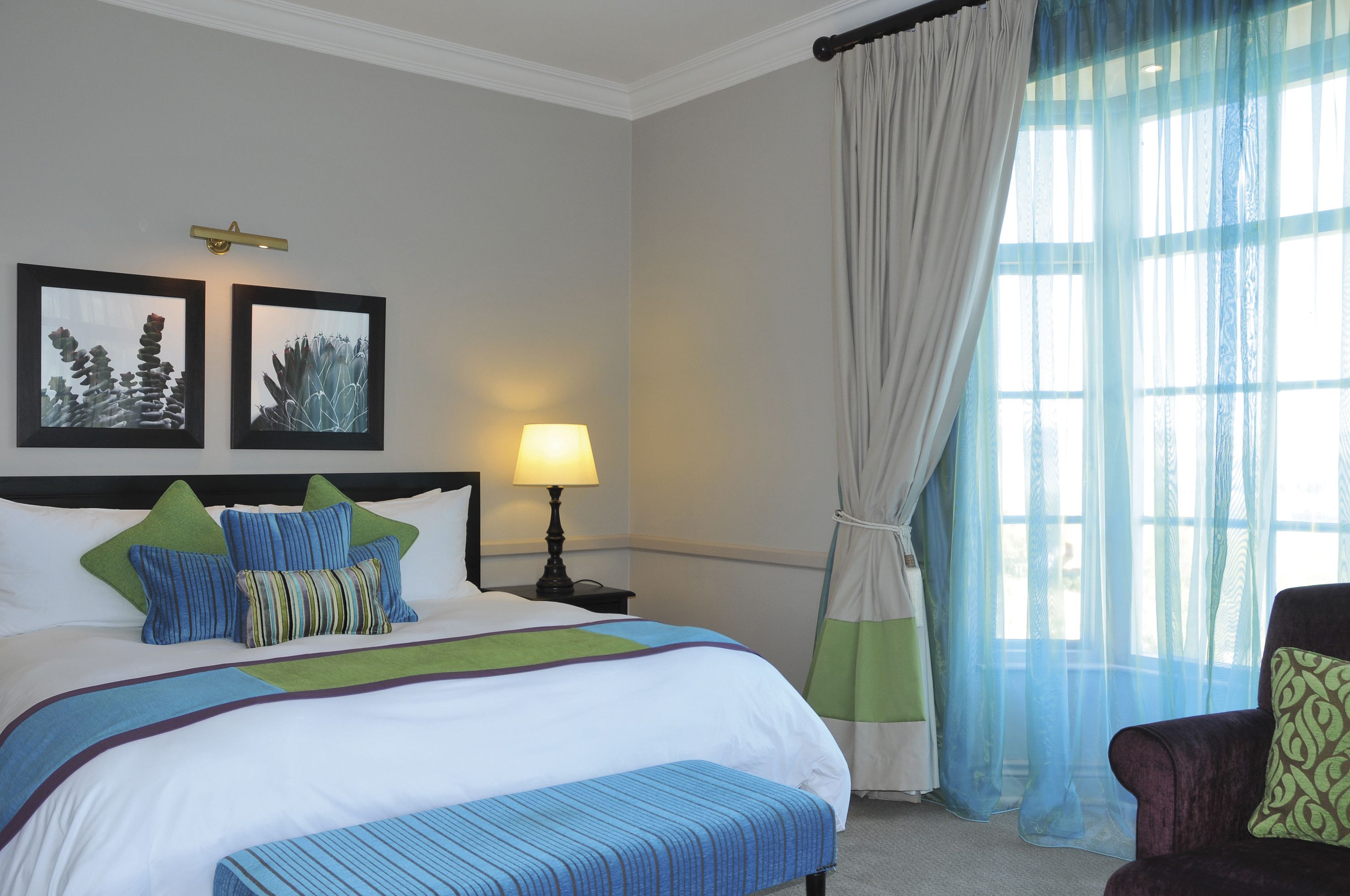 A neatly made bed with a green and blue striped pillow, a bedside lamp, and a framed picture on the wall.