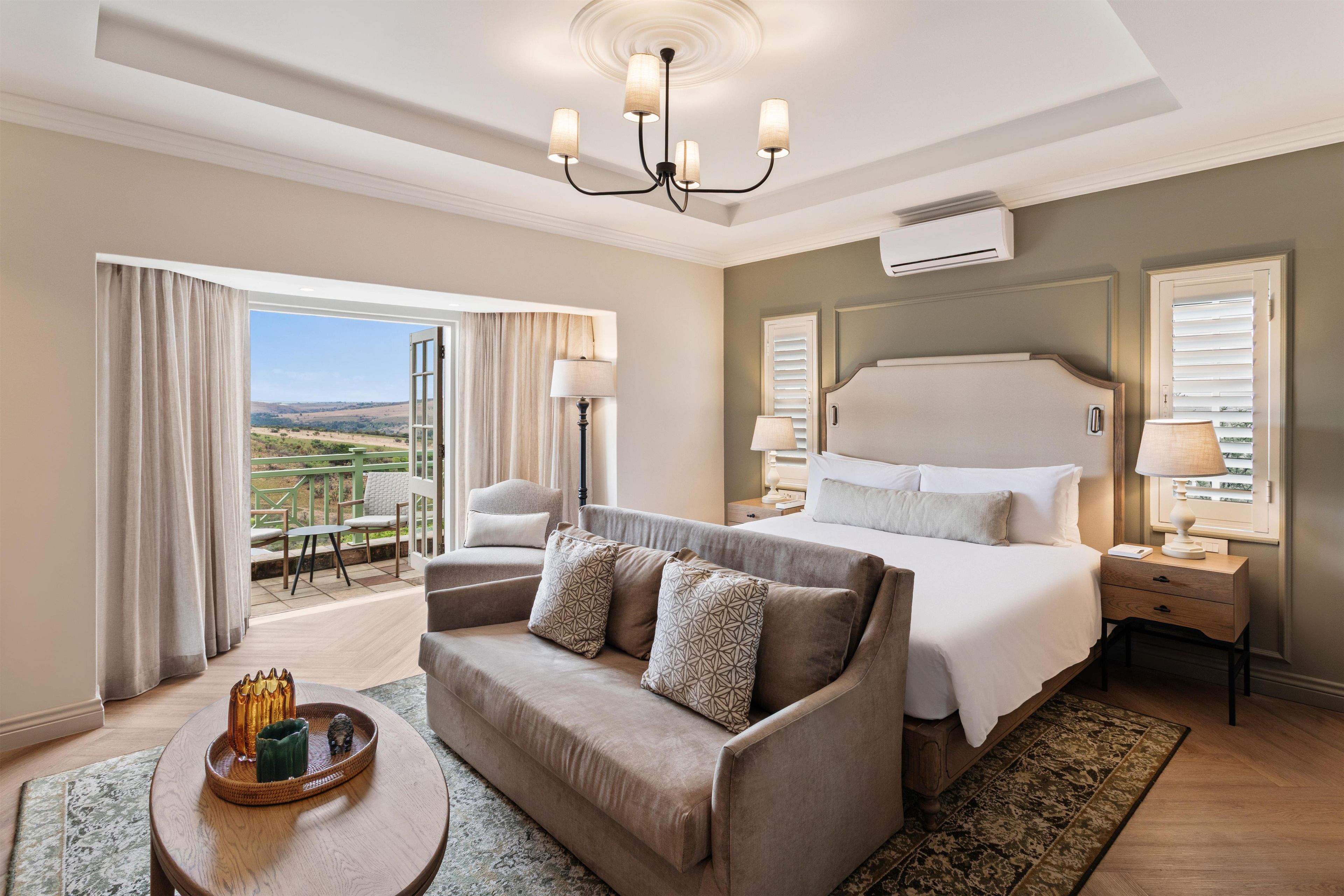 Habitación de hotel con una cama grande, un sofá, una mesa de comedor y vistas al exterior.