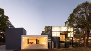A modern building with a staircase leading to a lit entrance, surrounded by trees and other buildings. - Ten Bompas (Randburg)