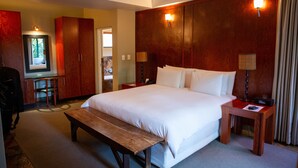 A hotel room with a large bed, wooden headboard, two bedside tables with lamps, a bench, a desk with a chair, and a mirror. - Ten Bompas (Randburg)