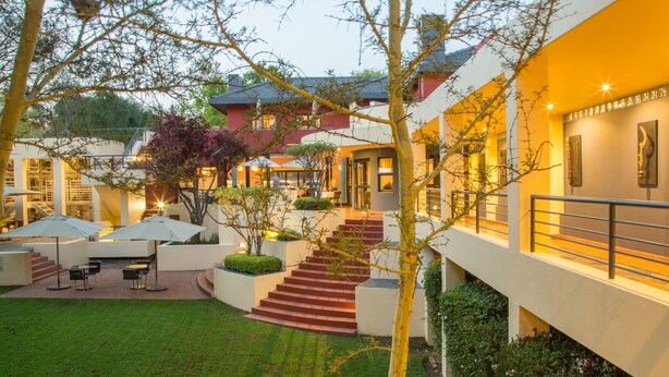 A hotel courtyard with outdoor seating, a staircase, and a building with a balcony. - Ten Bompas (Randburg)