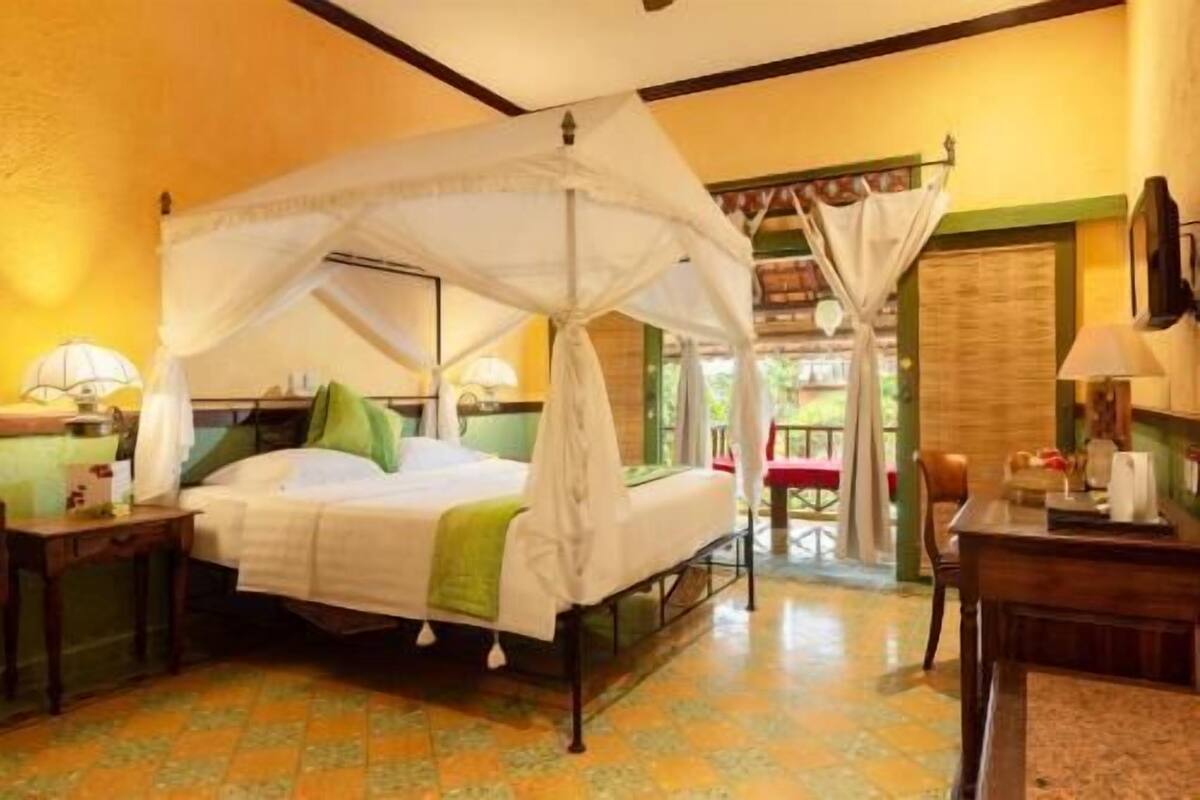 A room with a bed under a canopy, a desk with a chair, and a view of the outside.