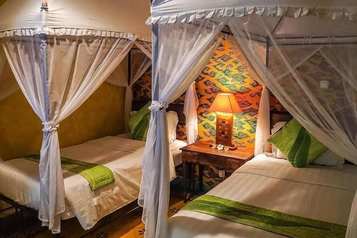 Two single beds with mosquito nets, a small table with a lamp, and patterned wall decor.